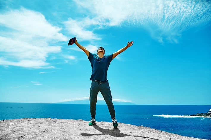 Happy guy on the beach with raised hands - looking to the blue sky