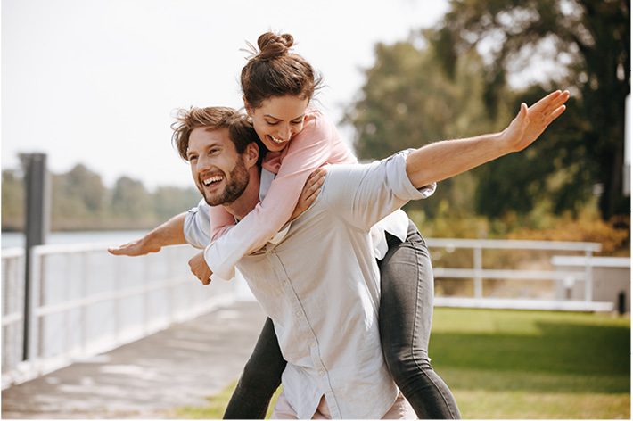 Young couple happy in the nature - guy carrying the girl on his shoulders