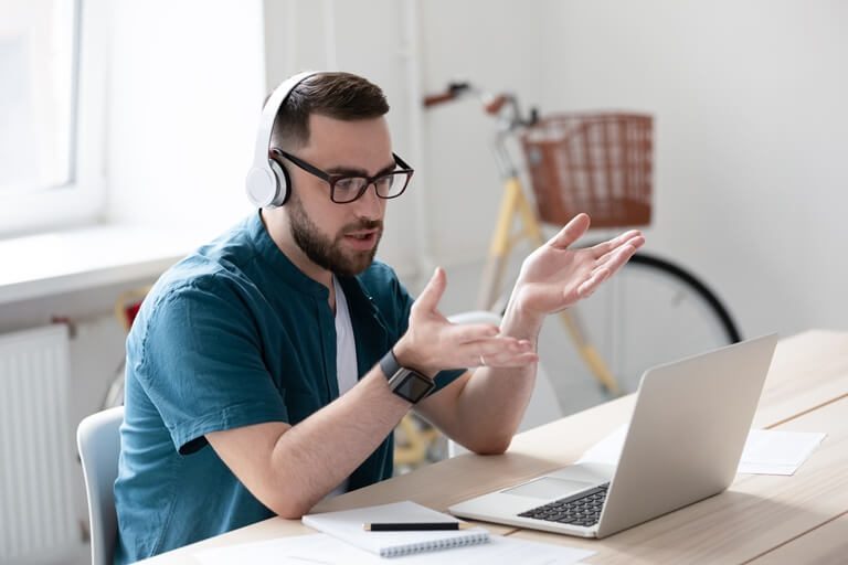 A young man with earphones, on a call on the laptop