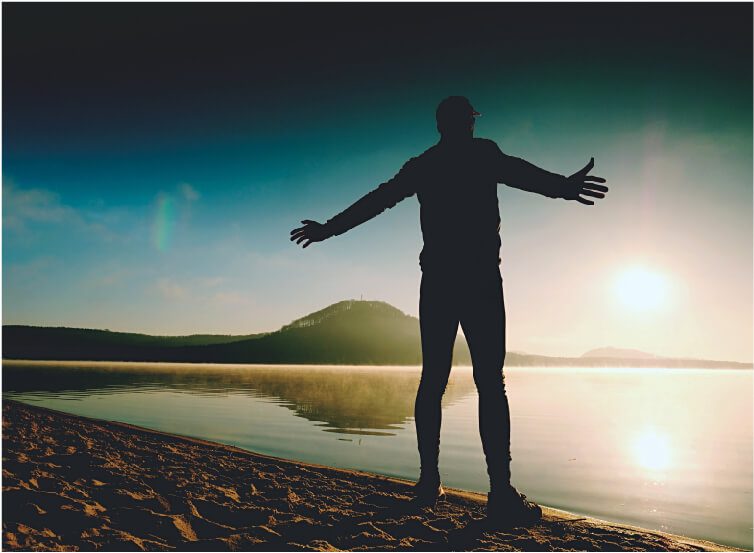 Person standing with raised hands on the beach during sunset